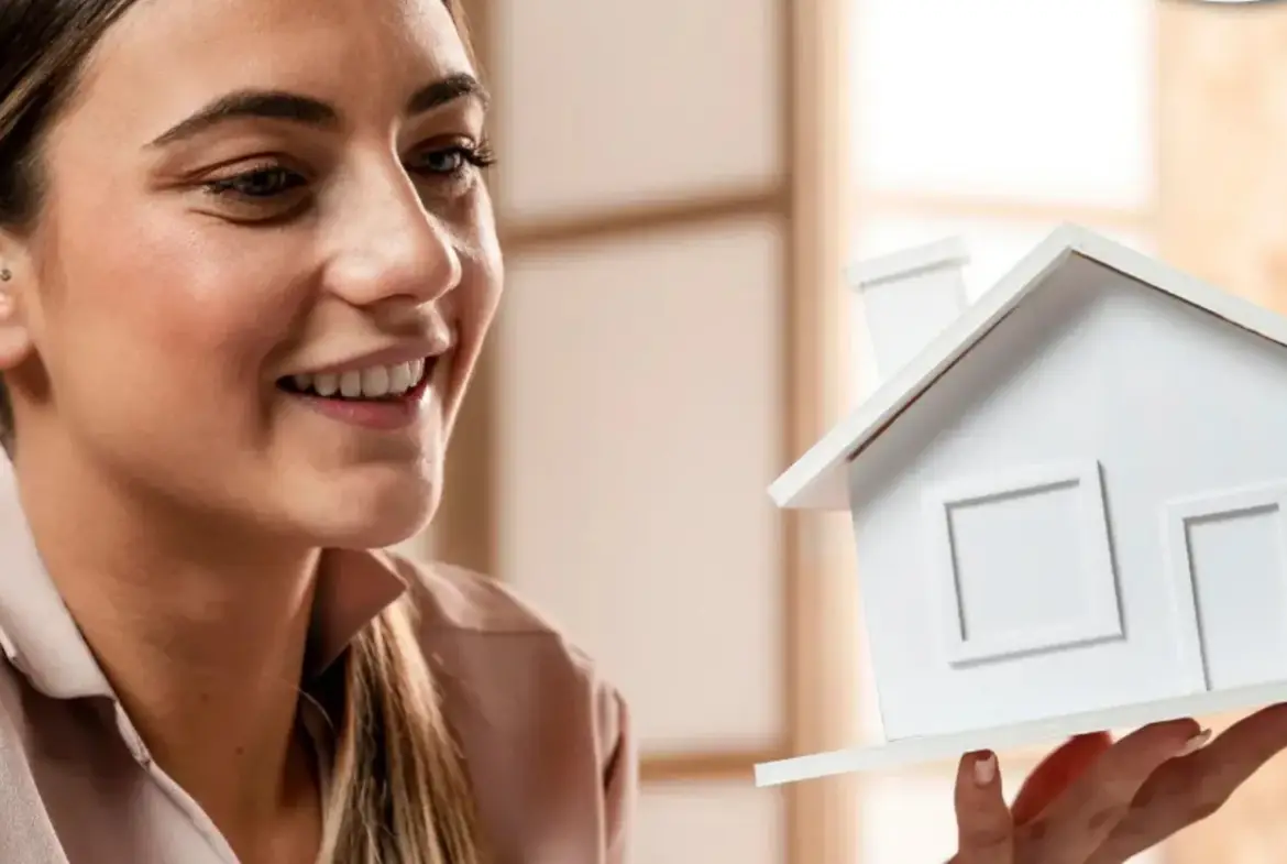 Mujer sonriente con un prototipo de casa en la mano.